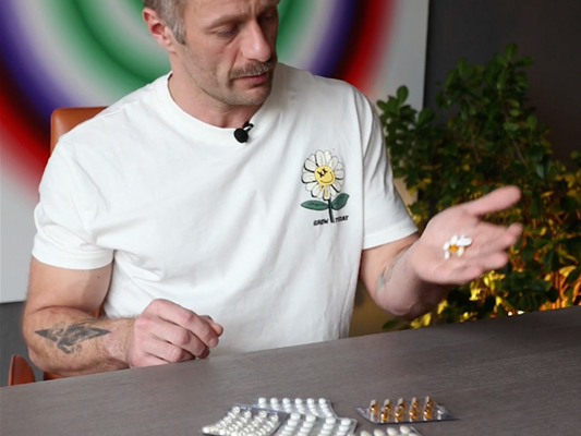 Mężczyzna prezentuje suplementy diety – różne kapsułki i tabletki na dłoni i stole, suplementacja dla dorosłych.