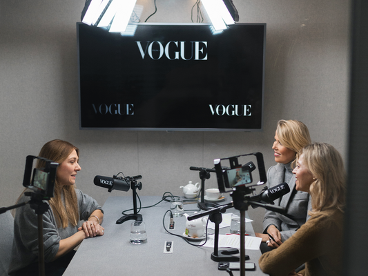 Trzy kobiety podczas nagrania podcastu w studio Vogue Polska – po lewej stronie Katarzyna Godlewska, współzałożycielka nikalab, rozmawia z dwiema prowadzącymi. Na stole mikrofony, filiżanki i notatki, w tle ekran z logo Vogue.