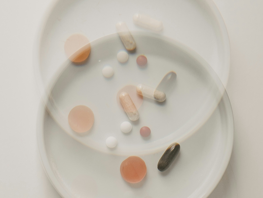 Artystyczne ujęcie suplementów diety na białych talerzykach – kapsułki, tabletki i żelki w stonowanych barwach, symbolizujące prostą i skuteczną suplementację od nikalab. Minimalistyczna kompozycja podkreślająca filozofię: mniej znaczy więcej.