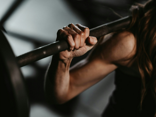 Zbliżenie na rękę kobiety trzymającej sztangę podczas treningu siłowego – ćwiczenia na siłę i wytrzymałość mięśni.