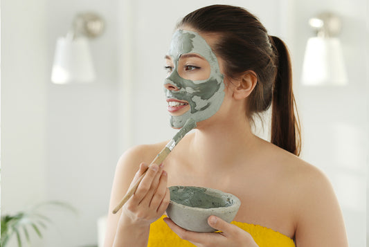Kobieta nanosząca na twarz maseczkę z kolorową glinką kosmetyczną