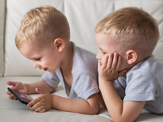 Dwóch małych chłopców skupionych na telefonie.
