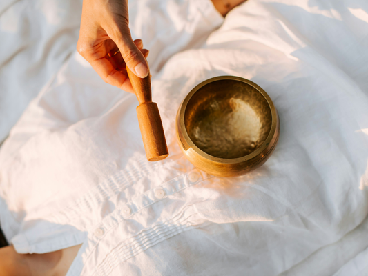 Mosiężna miska tybetańska trzymana nad białym materiałem – symbol spokoju i ciszy w świecie pełnym hałasu.