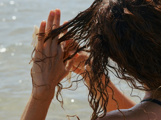 Kobieta nad wodą wciera odżywkę we włosy – symboliczna ilustracja artykułu o roli cynku w zdrowiu i kondycji włosów.