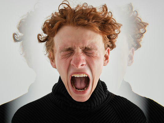 Młody mężczyzna z zamkniętymi oczami i otwartymi ustami, wyrażający intensywny krzyk – wizualna metafora gniewu i emocjonalnego napięcia