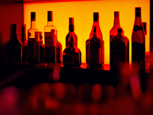Butelki alkoholu ustawione na półce w barze, podświetlone czerwonym światłem – ilustracja do artykułu o trendzie niepicia alkoholu i jego wpływie na zdrowie.