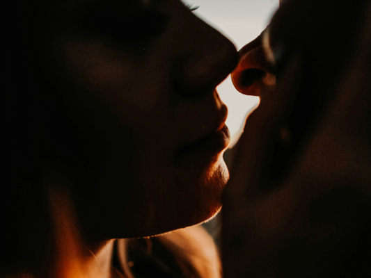 Zbliżenie dwóch osób w intymnym, czułym geście, twarze blisko siebie w półmroku.