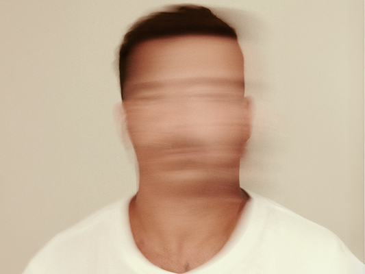 Rozmazana twarz mężczyzny w białej koszulce symbolizująca dezorientację i napięcie – ilustracja do artykułu o tym, jak stres wpływa na zdrowie psychiczne i fizyczne oraz jak się przed nim chronić.