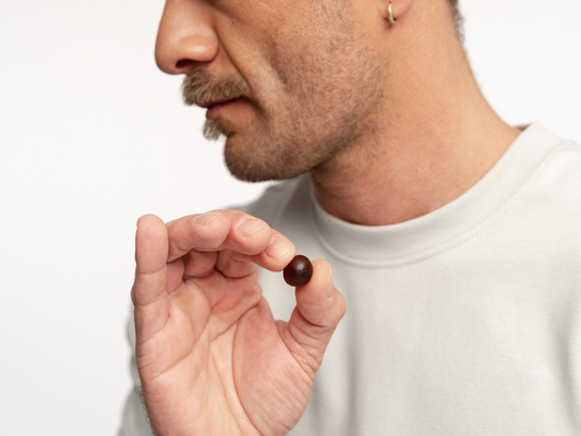 Mężczyzna trzymający w palcach pojedynczą żelkę suplementu diety Magnez + Witamina B6.