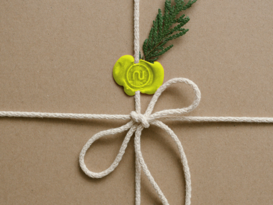 Naturalnie zapakowany prezent przewiązany jasnym sznurkiem, z zieloną pieczęcią i gałązką rośliny.