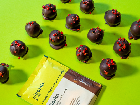 Wegańskie pralinki czekoladowe z białkiem, bez pieczenia, posypane różowym pieprzem, na zielonym tle obok opakowania odżywki białkowej nikalab.