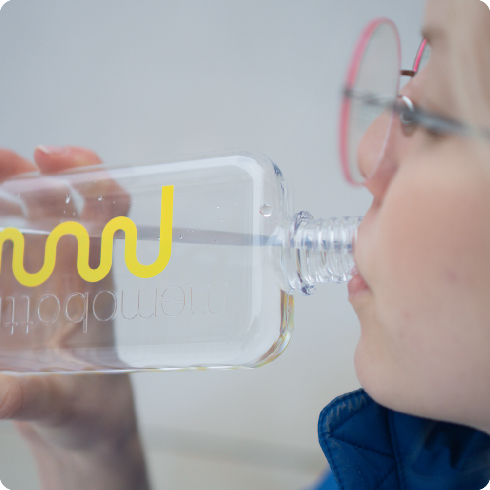 Osoba w okularach pije wodę z przezroczystej butelki memobottle z żółtym logo nikalab.