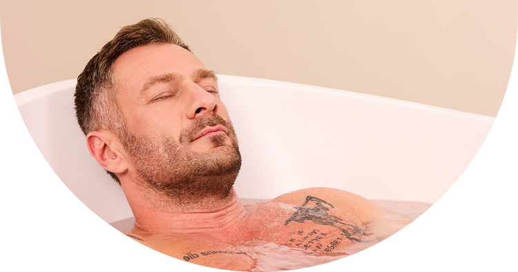 Mężczyzna relaksujący się w wannie podczas kąpieli z płatkami magnezowymi SPORT od nikalab, z zamkniętymi oczami i widoczną pianą na wodzie.