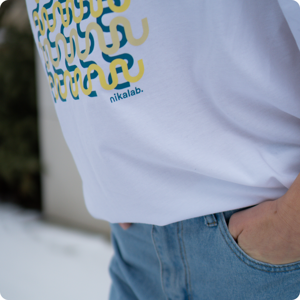 Zbliżenie na biały t-shirt z graficznym nadrukiem i logo nikalab oraz dłoń w kieszeni niebieskich jeansów.