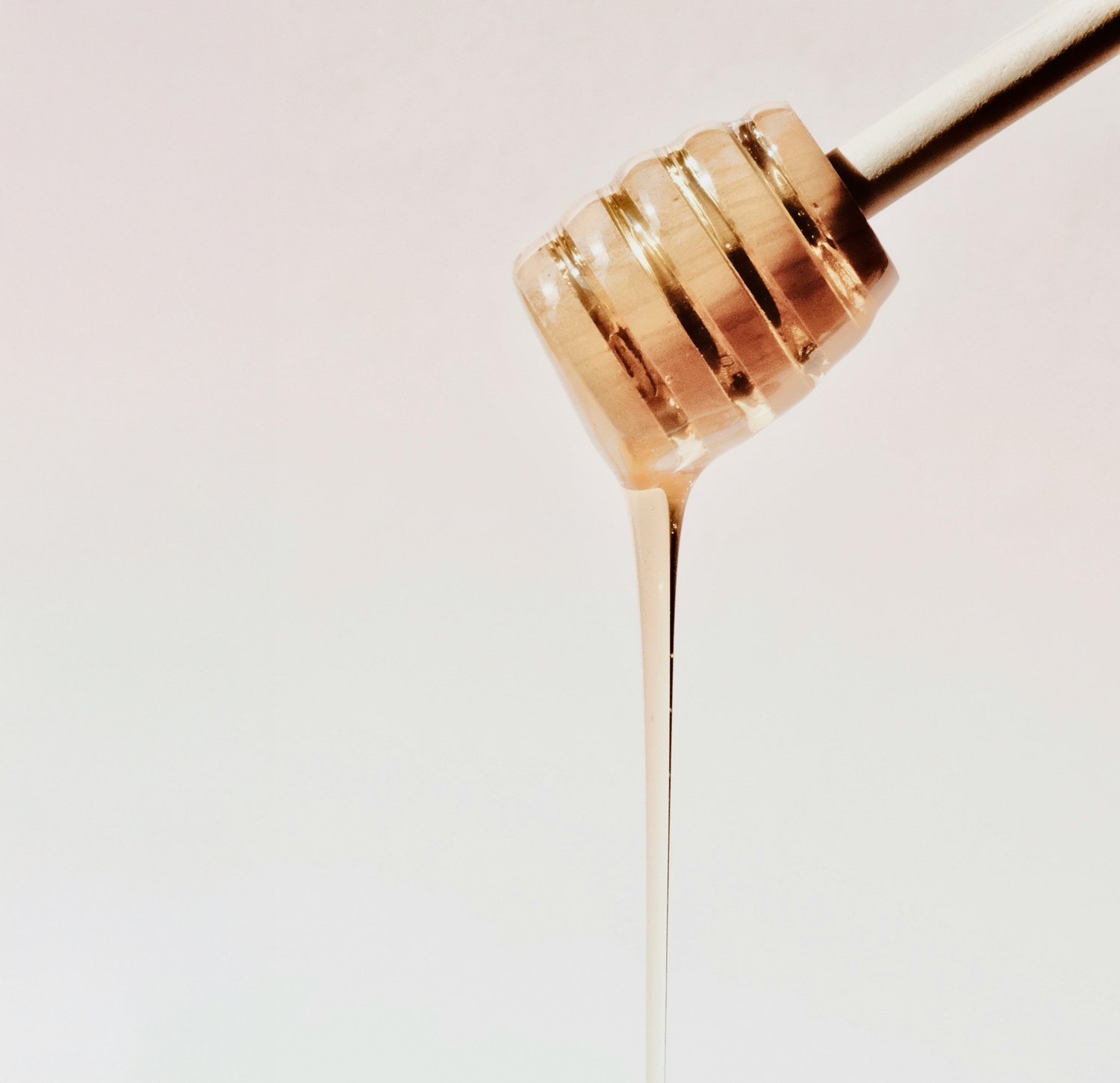 Naturalny syrop klonowy spływający z drewnianej łyżki na jasnym tle.