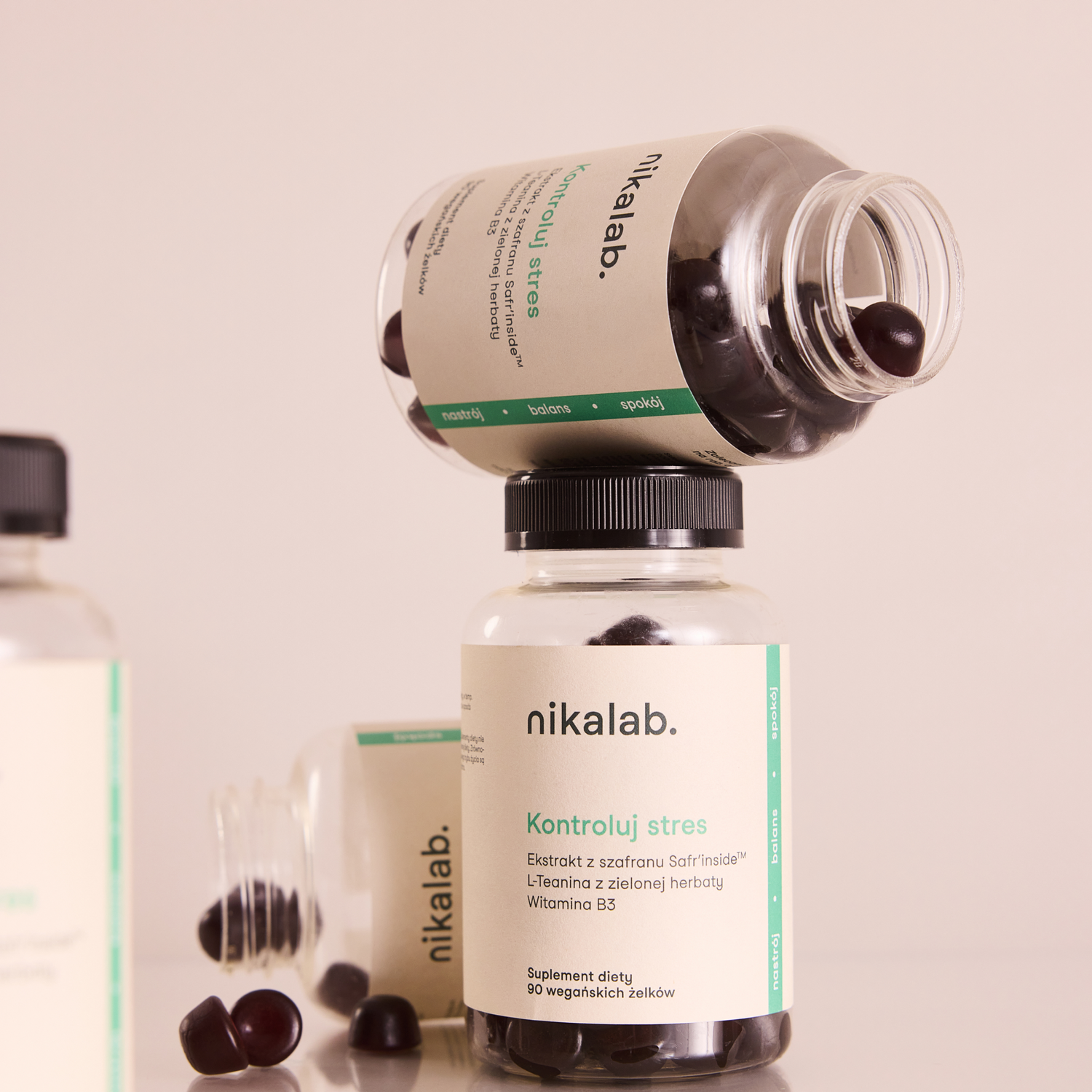 Słoiczki suplementu diety Kontroluj stres marki nikalab z wegańskimi żelkami, jedna ułożona poziomo na drugiej, z widocznymi kapsułkami na jasnym tle.