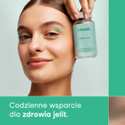 Uśmiechnięta kobieta trzymająca żywność specjalnego przeznaczenia medycznego od nikalab – Maślan sodu. Produkt wspiera codziennie zdrowie jelit i zawiera 60 wegańskich kapsułek.