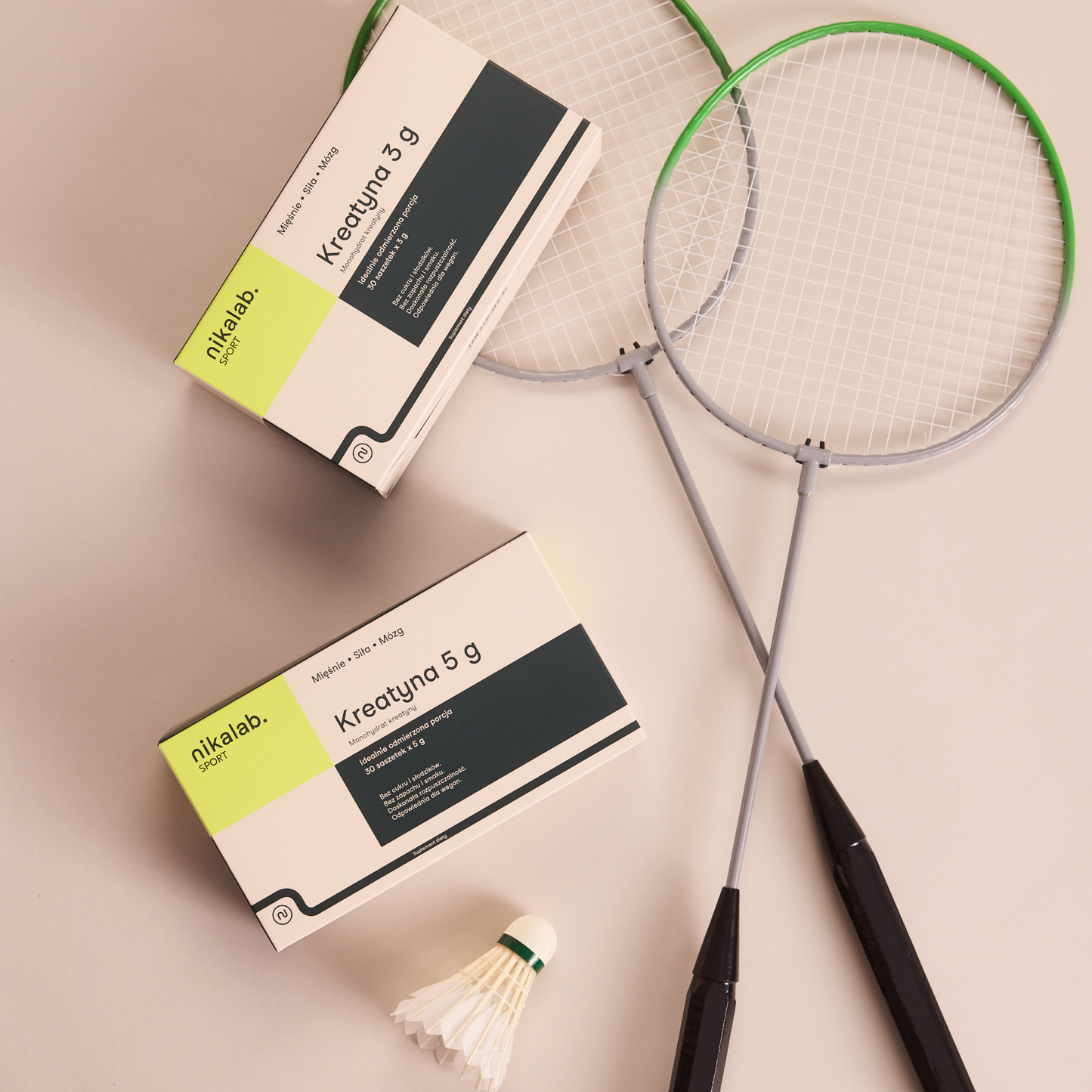Opakowania kreatyny nikalab sport w porcjach 3 g i 5 g ułożone obok rakiet do badmintona i lotki na jasnym tle.