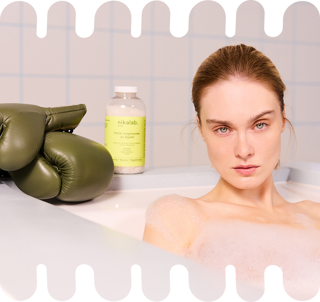 Kobieta w wannie z pianą po treningu, w tle widoczne opakowanie płatków magnezowych do kąpieli SPORT od nikalab oraz zielone rękawice bokserskie.