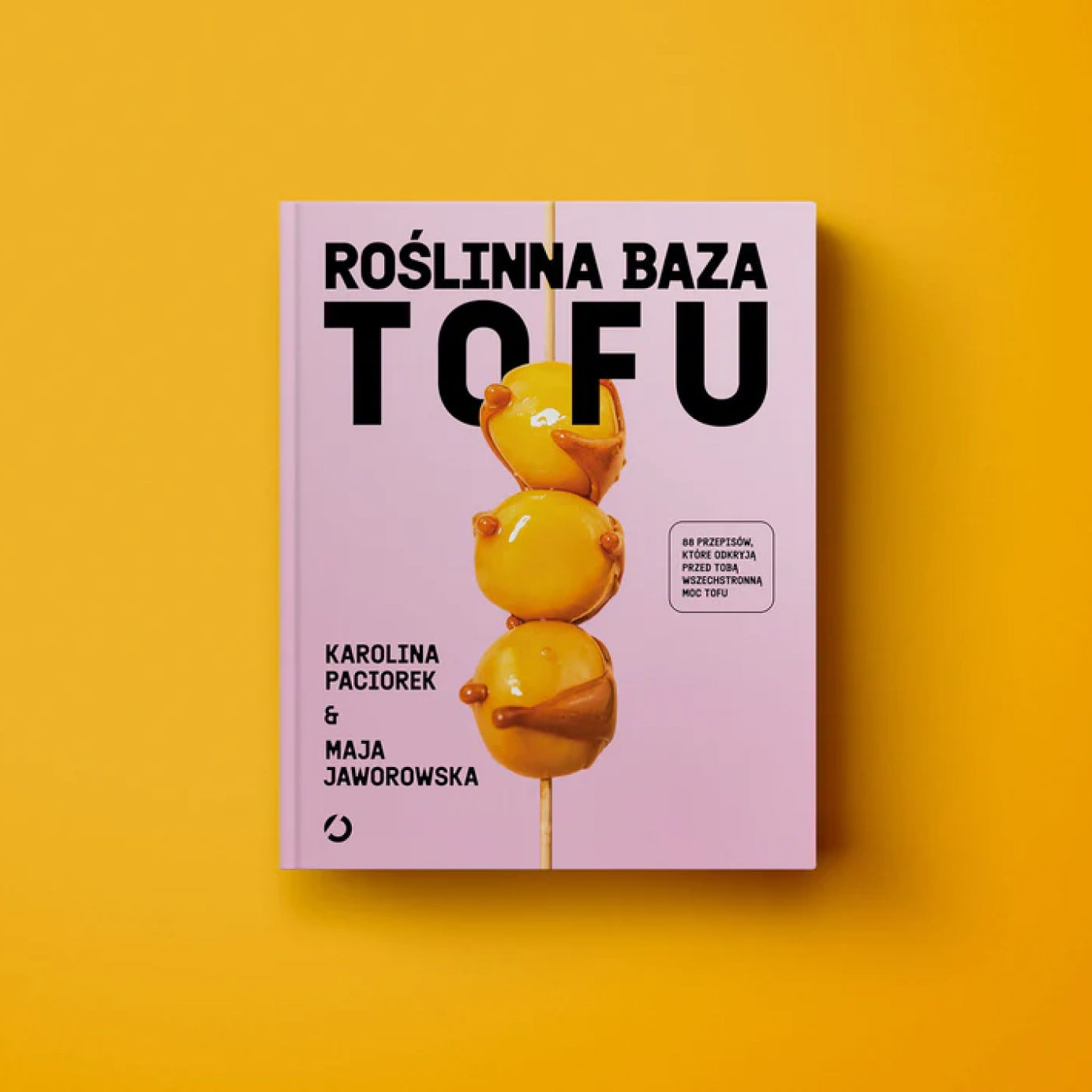 Okładka książki kucharskiej „Roślinna baza TOFU” autorstwa Karoliny Paciorek i Mai Jaworowskiej, z różowym tłem, żółtym tofu na patyku i tytułem promującym roślinne przepisy z tofu.
