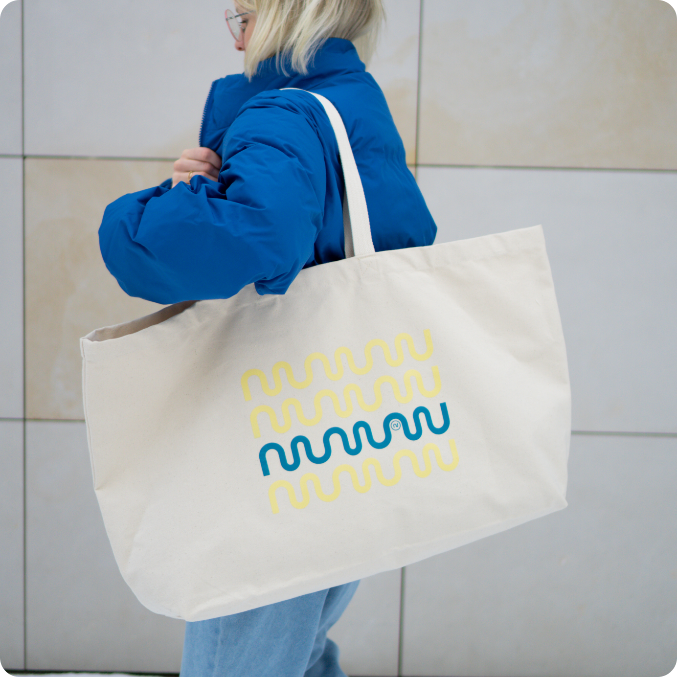 Osoba w niebieskiej kurtce niesie dużą bawełnianą torbę z kolorowym nadrukiem fali i logo nikalab.