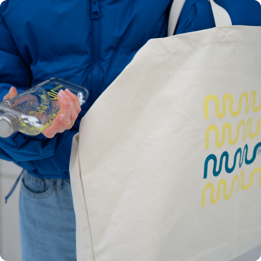 Osoba w niebieskiej kurtce trzymająca butelkę memobottle i dużą torbę z logo nikalab w graficzny wzór.