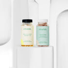 Zestaw dwóch suplementów diety nikalab: Baza na co dzień dla kobiet 50+ lat (60 wegańskich kapsułek) i Liposomalna witamina C (60 wegańskich kapsułek) – oba w biodegradowalnych słoiczkach z jasnymi etykietami.